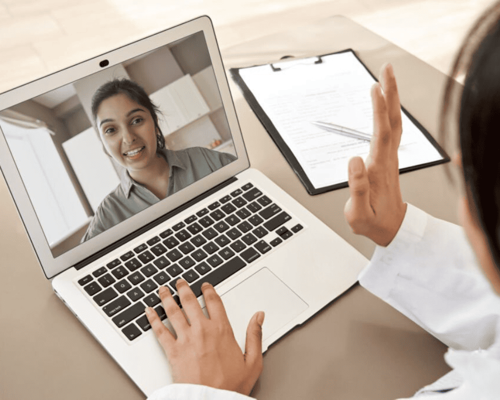 A person is engaging in a video call on their laptop, with one individual on screen smiling while the doctor raises a hand in greeting, seamlessly utilizing HMIS technology for an enhanced A person is engaging in a video call on their laptop, with one individual on screen smiling while the other raises a hand in greeting, seamlessly utilizing HMIS technology for an enhanced communication experience.A person is engaging in a video call on their laptop, with one individual on screen smiling while the other raises a hand in greeting, seamlessly utilizing HMIS technology for an enhanced communication experience.